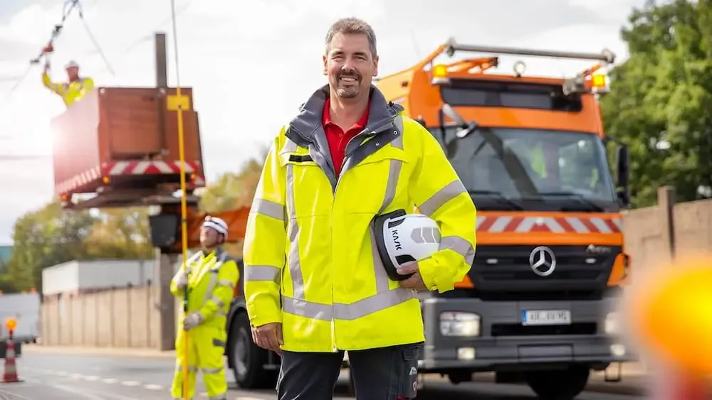 Kollege in gelber Warnjacke vor Oberleitungswagen