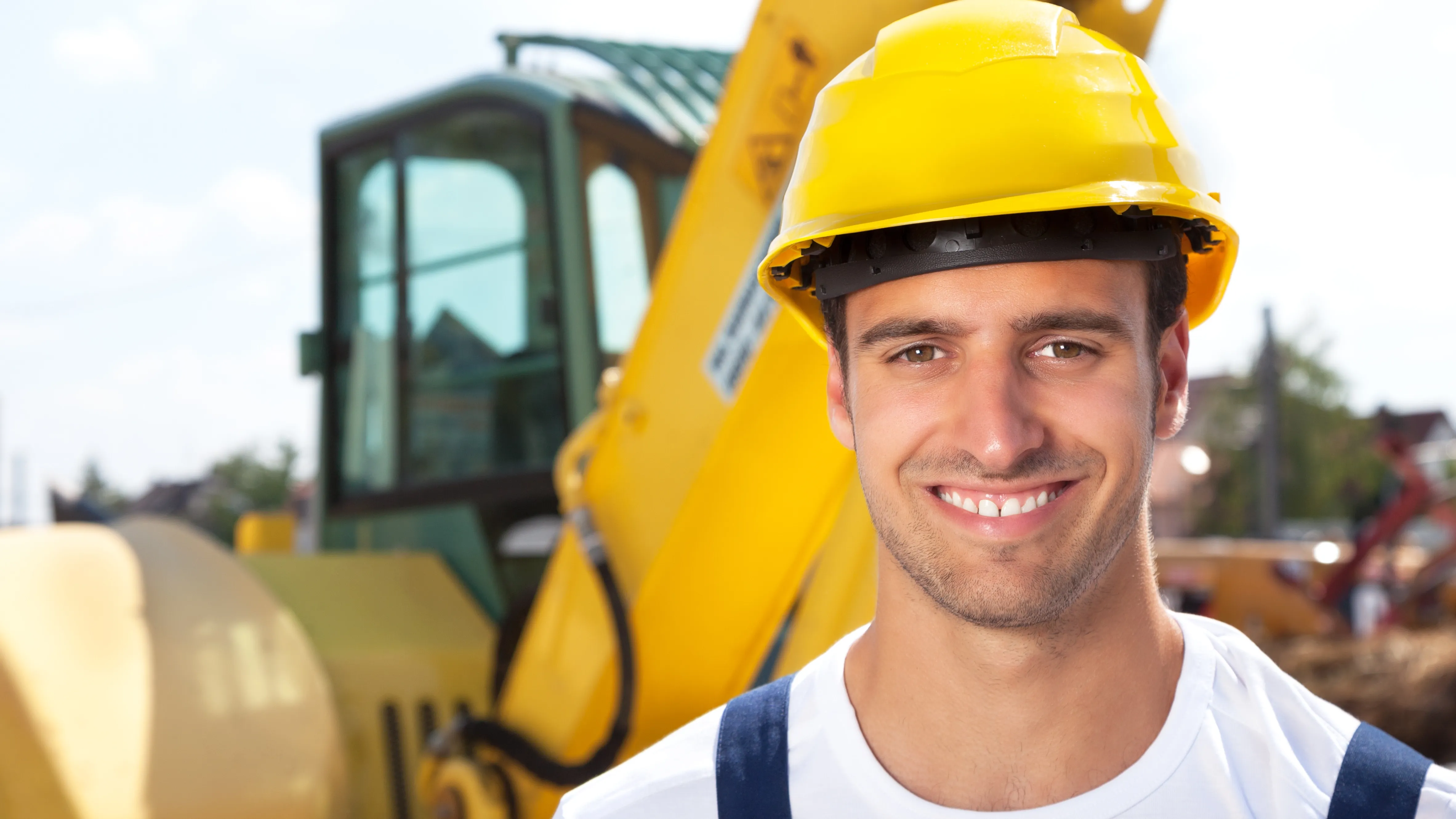 Junger Mann in Arbeitskleidung und Helm lächelt in die Kamera