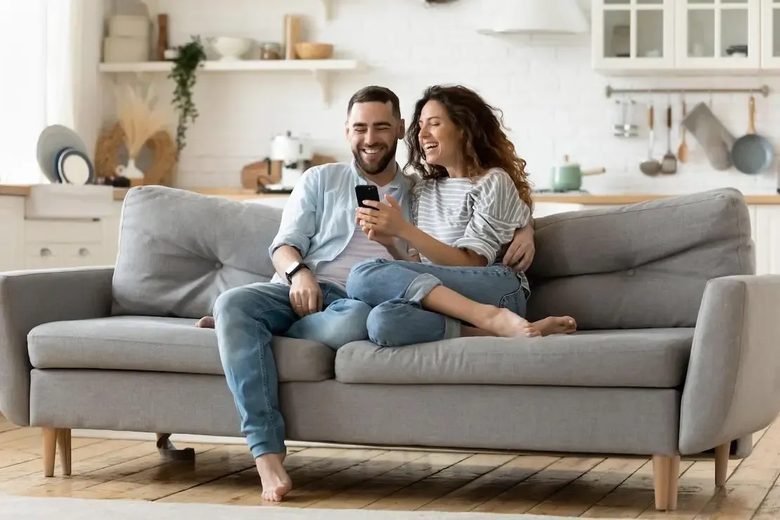 GSAK Pärchen sitzt lachend auf dem Sofa und schaut auf das Smartphone