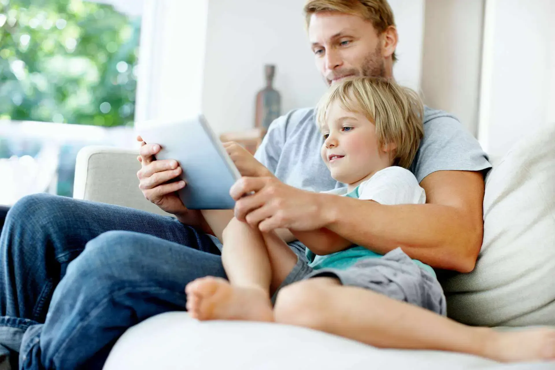 Vater und Sohn sitzen auf der Couch und schauen aufs Tablet