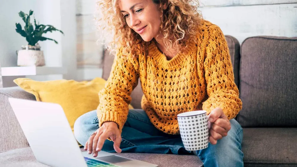 Frau sitzt mit Laptop auf der Couch und surft auf der Webseite der SWK